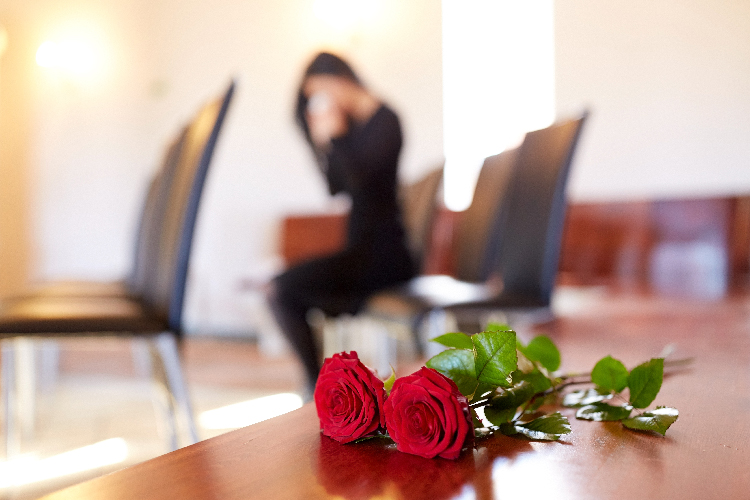 people and mourning concept - red roses and woman crying at funeral in church